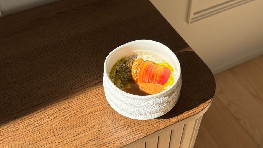 Kulhollinen chiavanukasta persikoilla, mantelivoilla, hampunsiemenill ja avokadoljyll on asetettuna lipaston plle.