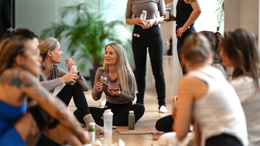 Ryhm� naisia istuu joogamatoilla valoisassa huoneessa ja juttelee samalla nauttien terveellist� v�lipalaa ja juomia.