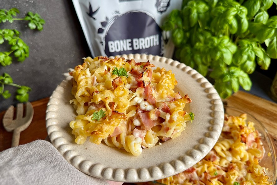 Lautasellinen pastavuokaa, Taustalla Healthwell Luuliemi -pussi, pastavuoka, puinen haarukka ja basilika.