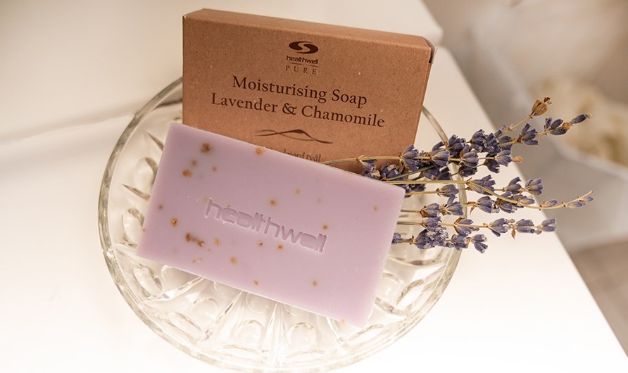 Healthwell PURE Moisturising Soap Lavender & Chamomile, sen kartonkipakkaus ja laventelinoksa lasikulhossa.