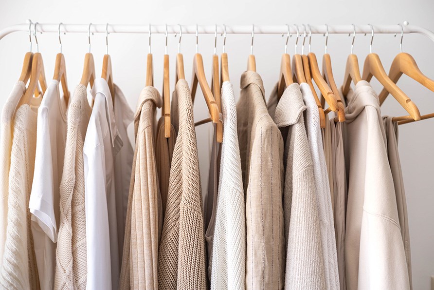 Vaaleita neuleita ja paitoja puisilla henkareilla roikkumassa rekillä. Vaaleita neuleita ja paitoja puisilla henkareilla roikkumassa rekillä.