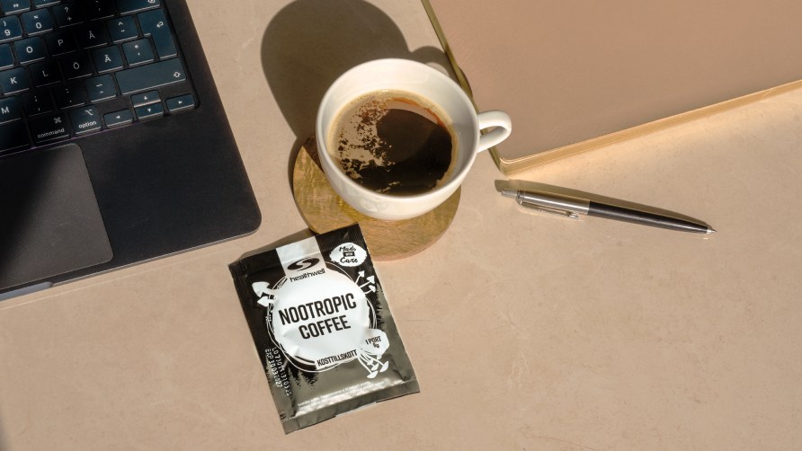 Yksi Healthwell Nottropic Coffee -pussi ja kupillinen kahvia p�yd�ll�. Vieress� tietokone, kyn� ja vihko.
