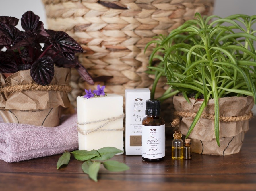 Pure argan oil stands with the box, plants and a soap in front of a basket.