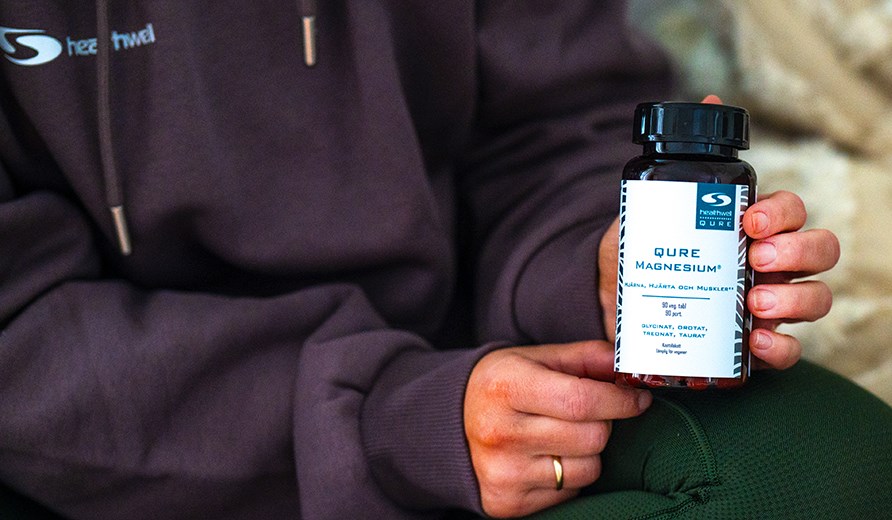Kuva kahdesta kdest, jotka pitvt Healthwell QURE Magnesium -purkkia.