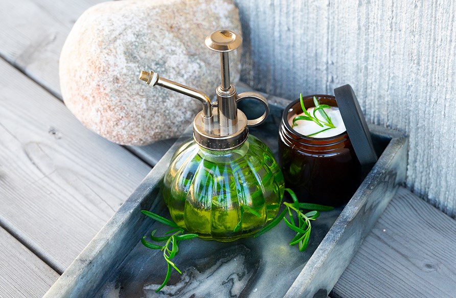 Rosmariinivett lasisessa suihkepullossa ja rosmariinihiusnaamio purkissa.