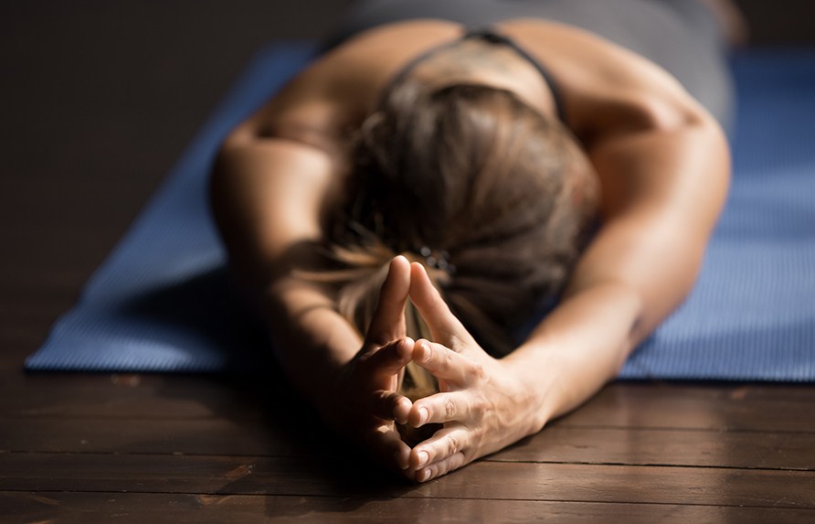 Nainen vatsallaan joogamatolla kdet yhdess pn ylpuolella kuvattuna ksien suunnasta.