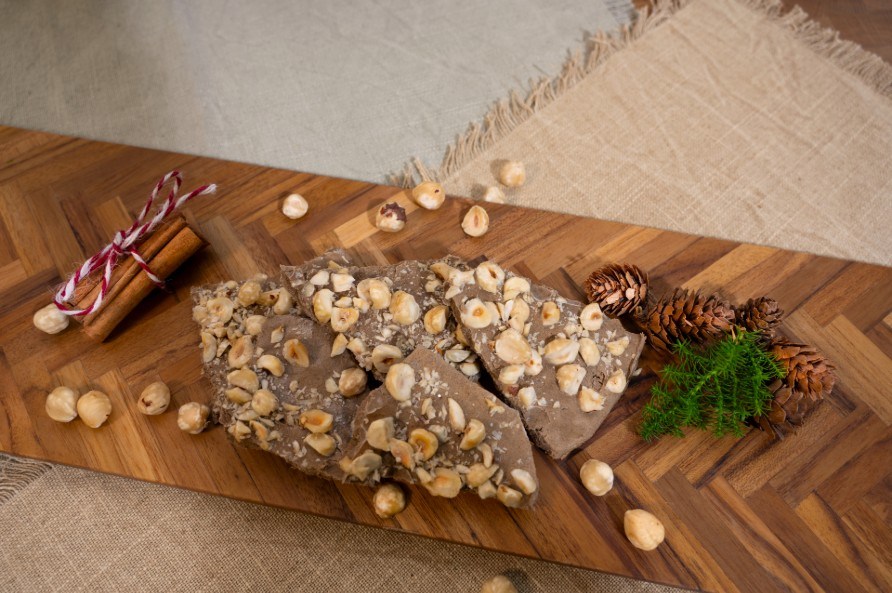 Jouluisen jogurttilevyn paloja leikkuulaudalla kanelitankojen, kpyjen ja hasselphkiniden kera.